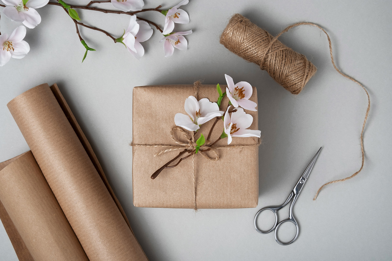 En gavepakke med blomster og brunt papir, saks og snor på en lys bakgrunn