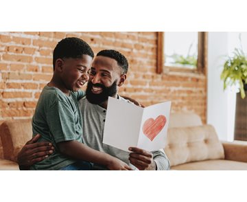 Far som holder hvit kort med rød hjerte fra sønnen sin som sitter på fanget hans