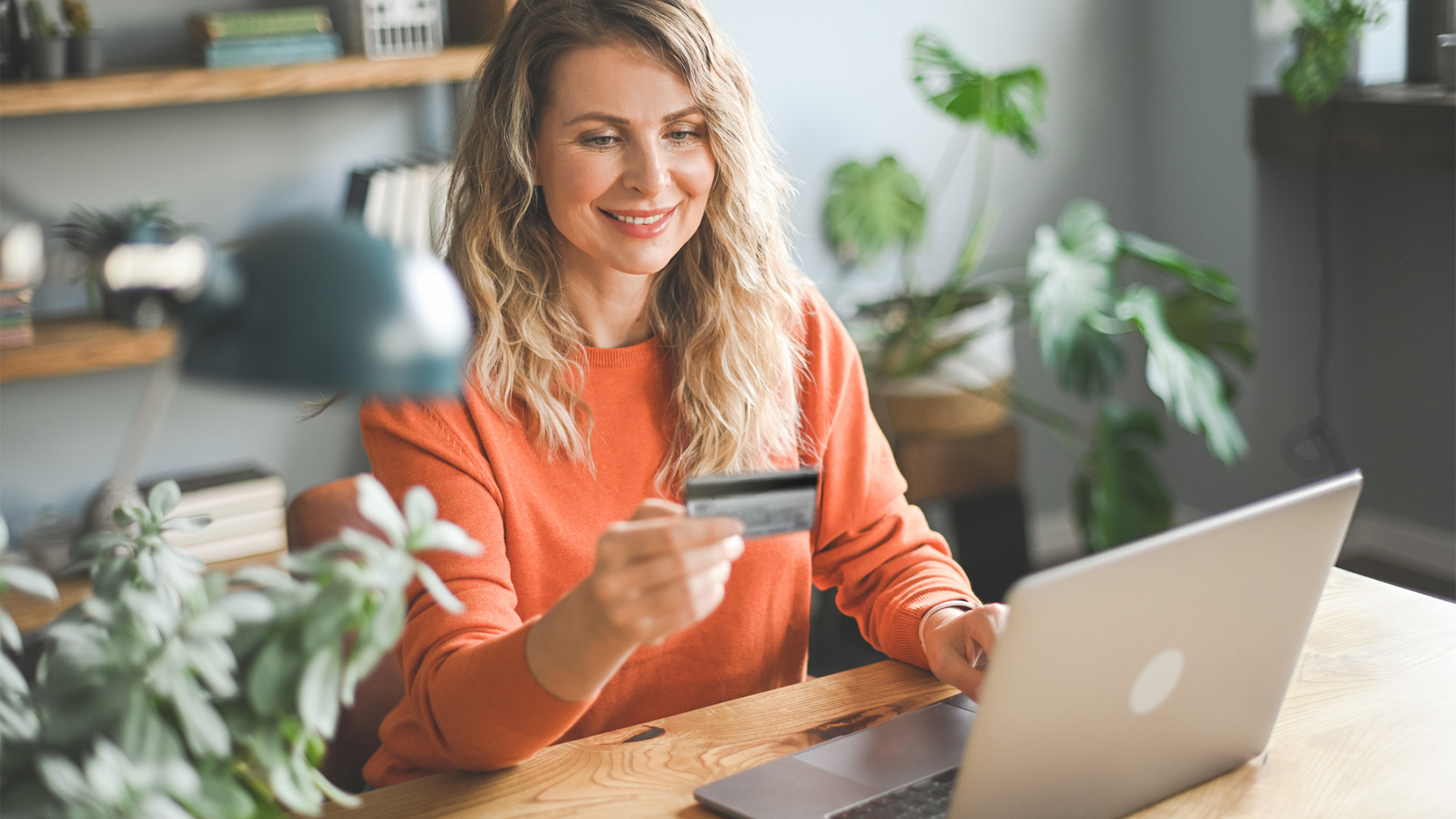 Dame som holder et gavekort mens hun sitter foran pc en sin