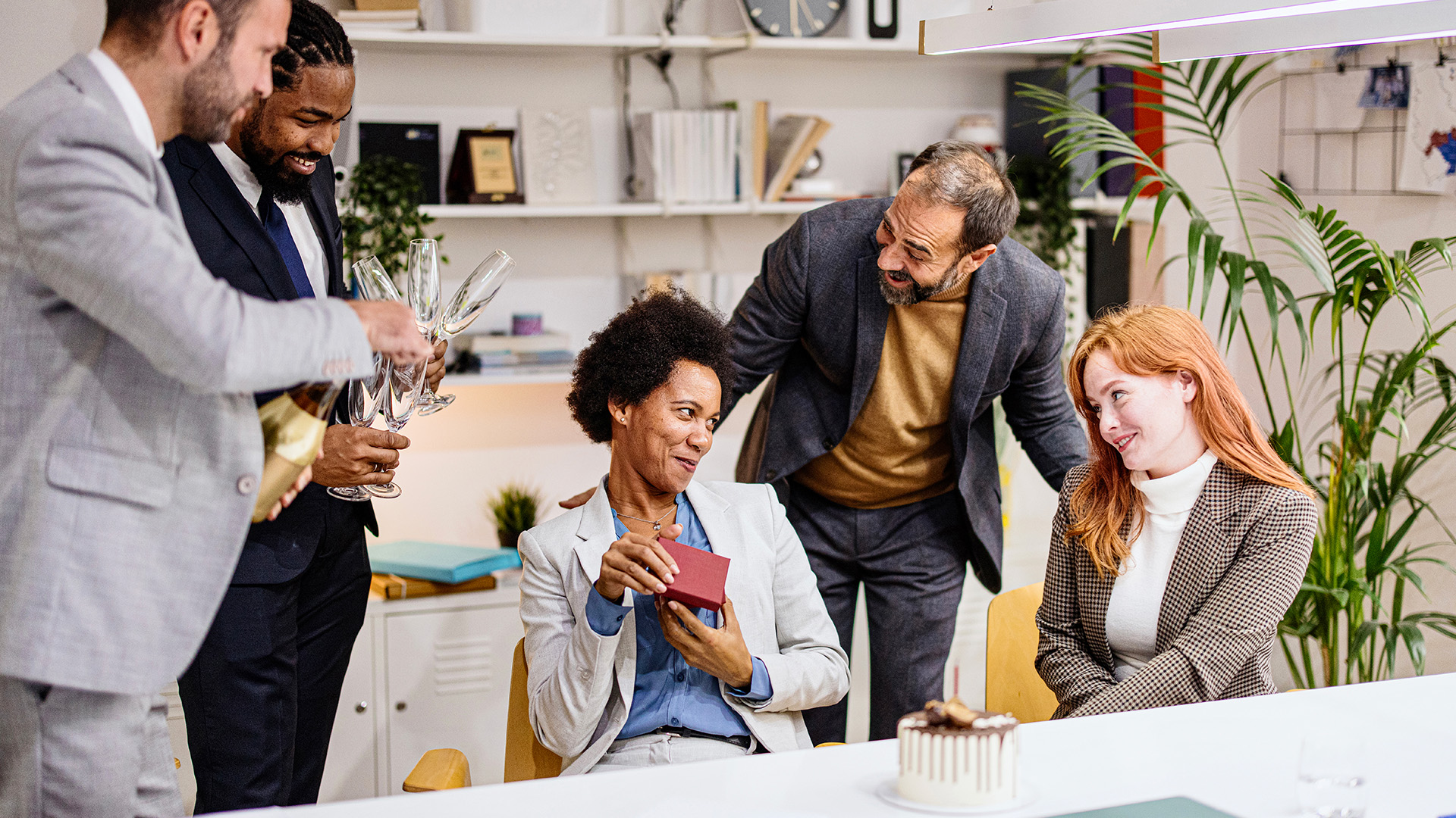 En kvinne åpner en gave mens kollegaer står og ser på. .