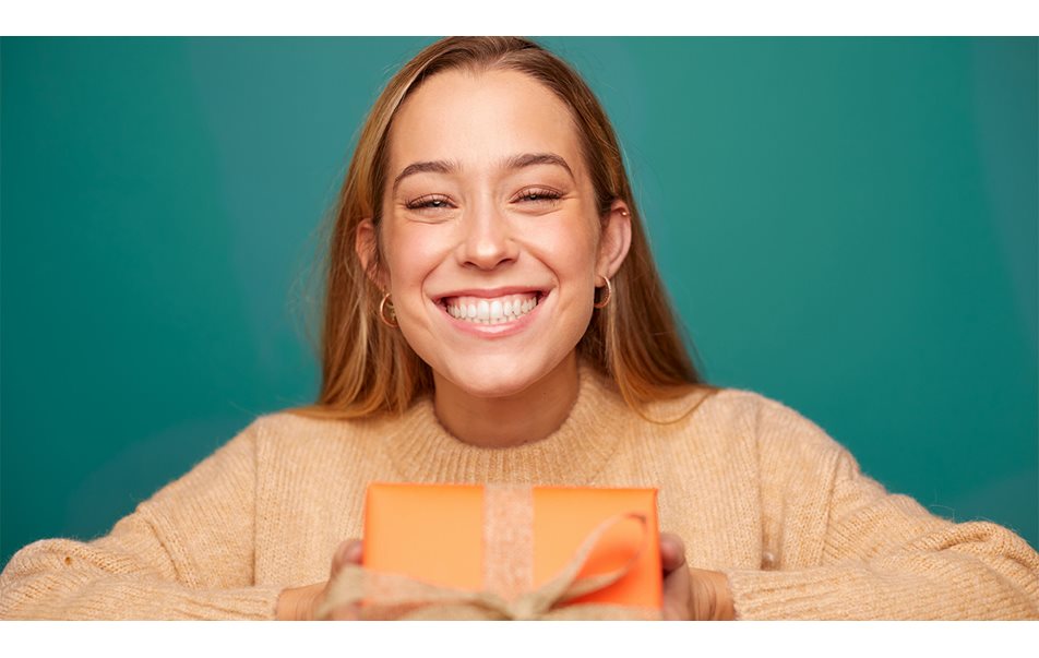 smilende jente i oransje genser som holder en oransje gaveeske