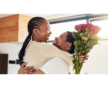 Bilde av et par som smiler og klemmer hverandre hvor damen holdet et bukett med røde roser